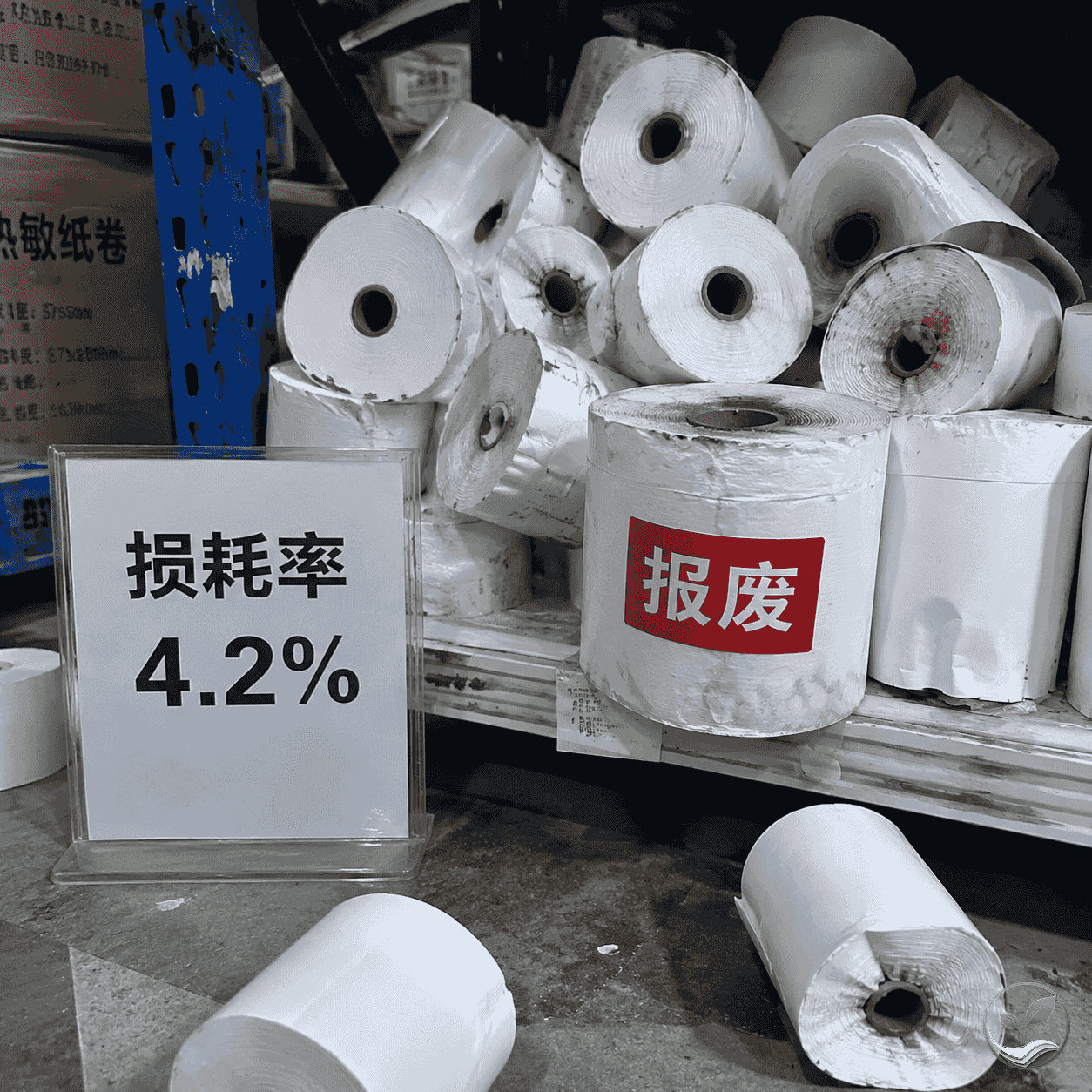 仓库中一堆积压受潮的收银纸卷,部分纸卷变形,旁边有报废标签和损耗率4.2%的数据牌